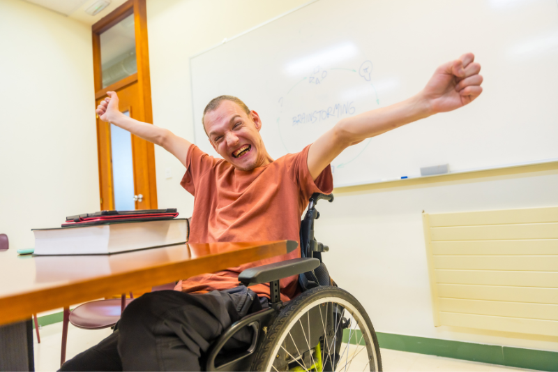 un hombre en silla de ruedas abre los brazo en un aula